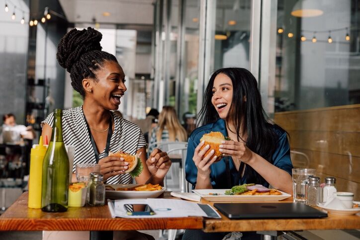 Two businesswomen eating hamburger at lunch break
