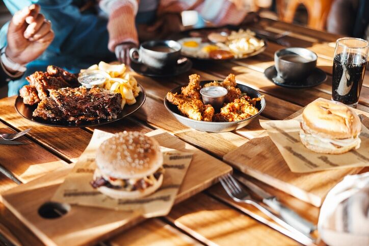 Fast food, lunch or dinner on table at restaurant, people eating for nutrition and wellness with time together Catering, hospitality and cuisine with burger, chicken and ribs for protein at diner